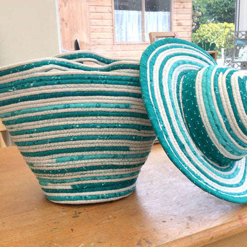 Teal and white striped basket and coiled rope hat on a wooden surface