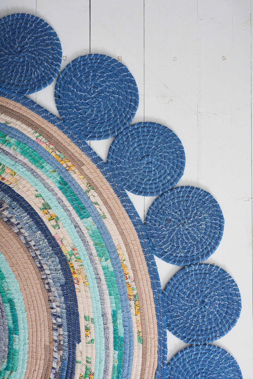 Round coiled rope zig zag stitched handmade rag rug with blue circular patterns on a light wooden floor.