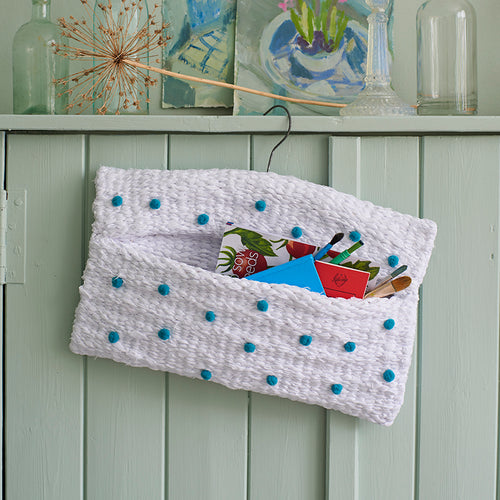 White and blue peg loom weaving turned into a storage bag. Made using white cotton sheets and pom poms. Peg loom project from Rag Rug Techniques for Beginners.