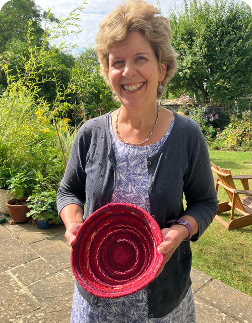 Woman holding a red coiled rope bowl outdoors in a garden setting