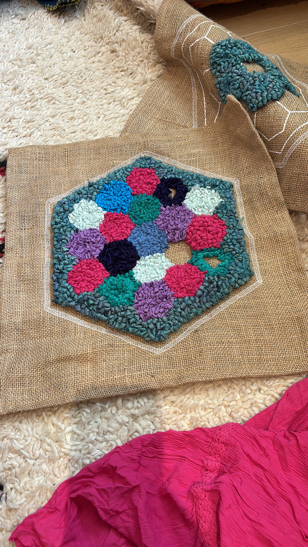 Hexagonal rug hooked patch with colorful patchwork pattern on a rug with fabric and other projects around