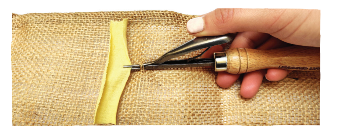 Hand using a rag rug spring tool to pull a piece of fabric through a burlap rug backing