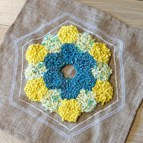 Hexagonal rag rug mat with blue and yellow flowers on a brown 10 holes per inch hessian rug backing