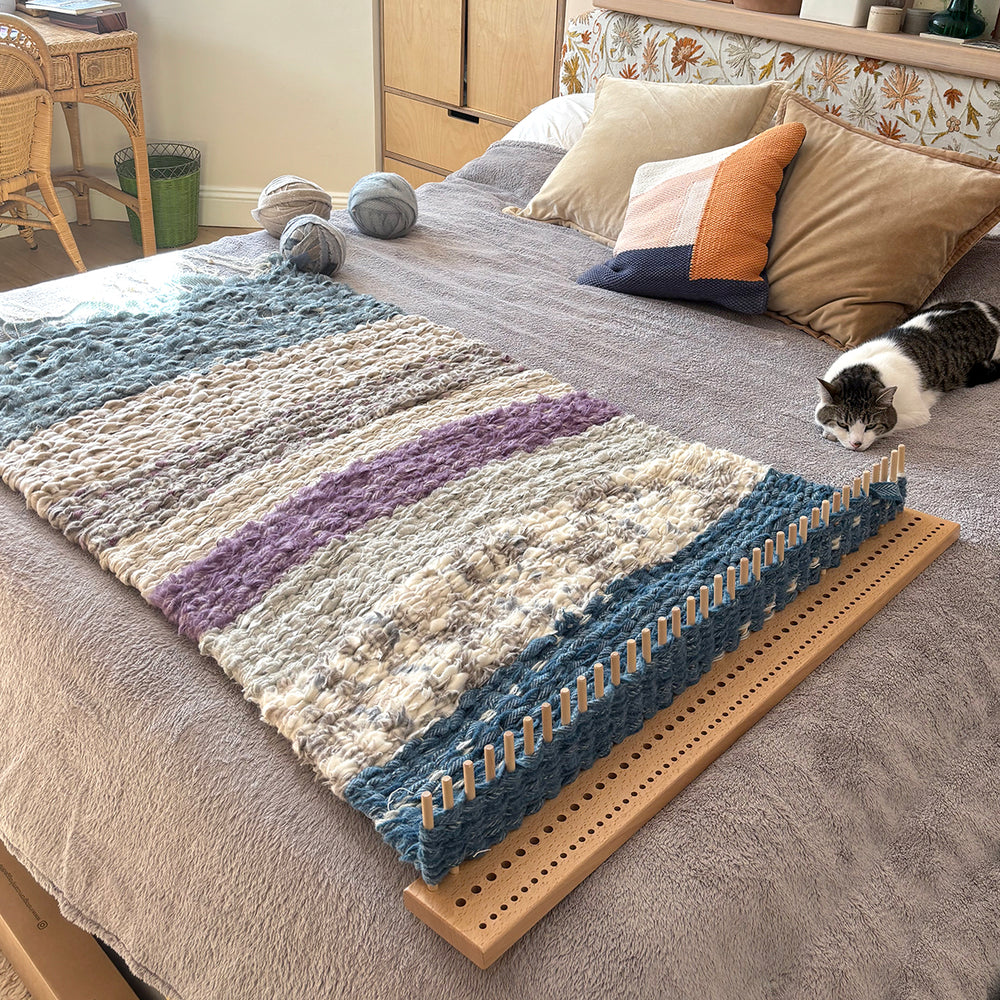 Work in progress extra large peg loom rug on a large wooden peg loom on the bed with balls of woollen fabrics strips for weaving