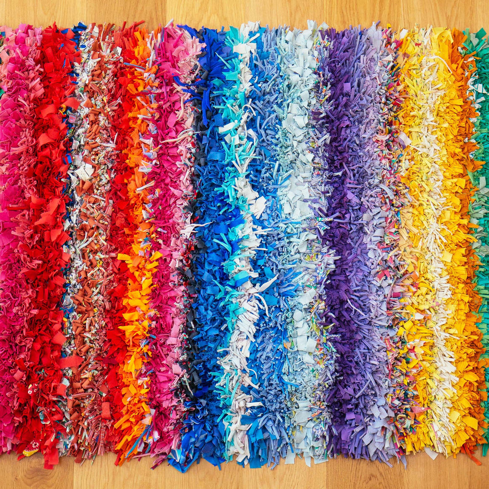 Shaggy rag rug with a colourful rainbow stripe pattern displayed inside on a wooden floor